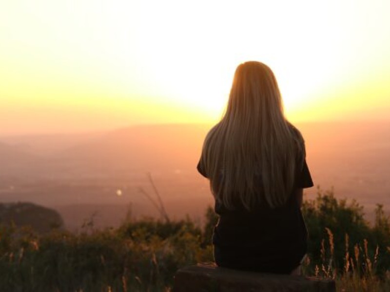 A person with long hair sits looking at a sunny horizon line