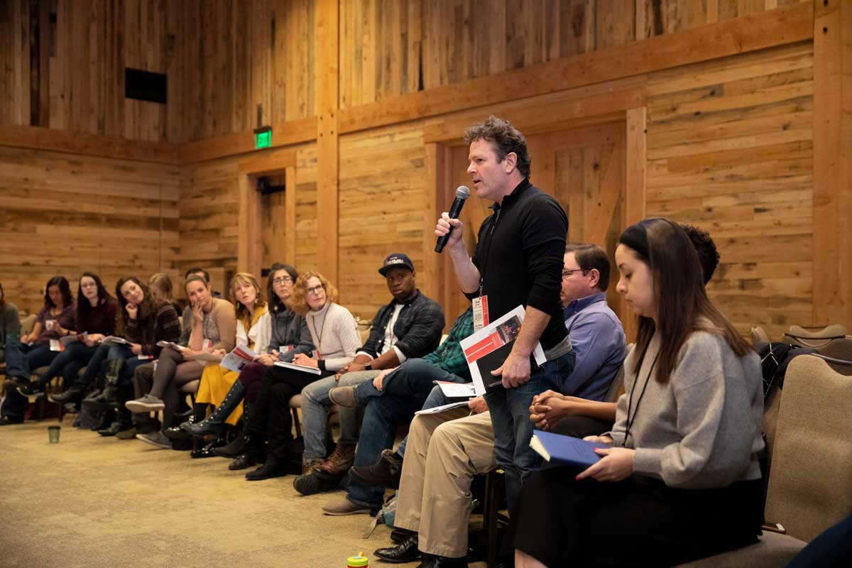 A standing person speaks into a microphone at a meeting