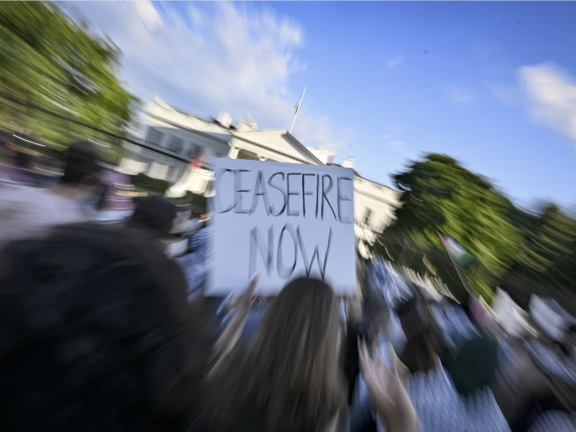 Photo by Celal Gunes/Anadolu via Getty Images shows a crowd in front of the White House. One person holds a sign with "Ceasefire Now" written on it.