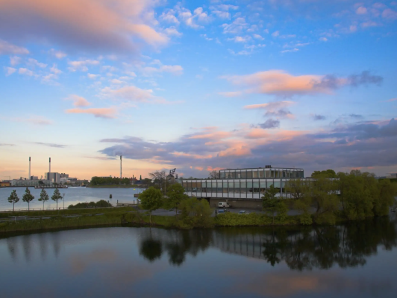 Clouds shine brightly over a modern office building surrounded by trees and water