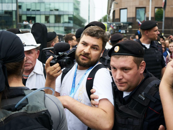 A police officer holds a news photographer by the arm in a crowd