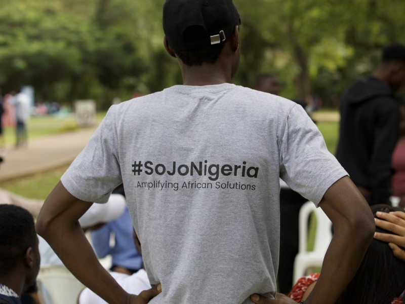 A man stands with hands on hips. His shirt reads "#SoJoNigeria, Amplifying African Solutions"