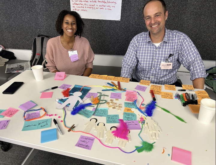 Two Beacon Cohort participants sit at a table covered in sticky notes and pens