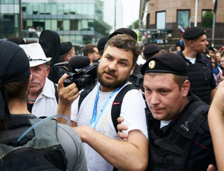 A police officer holds a news photographer by the arm in a crowd