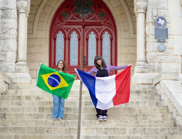 Two women hold flags on the steps of a university building